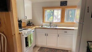Una cocina con armarios blancos, estufa, lavamanos y ventana con vistas a árboles.