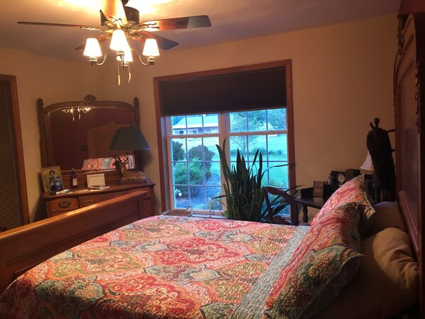 Un dormitorio con una cama grande, un aparador, un espejo, un ventilador de techo y una ventana con vistas al exterior.