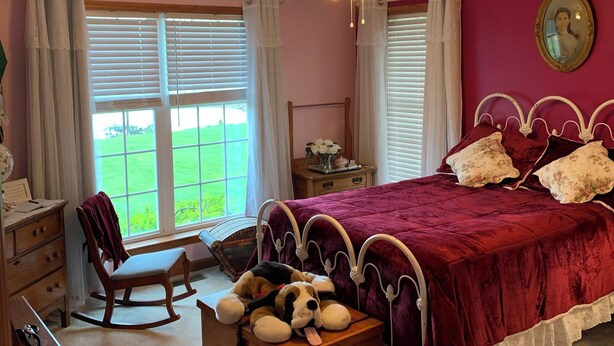 Une chambre à coucher comprenant un lit, une commode en bois, un fauteuil à bascule, un bureau et une fenêtre avec des stores.