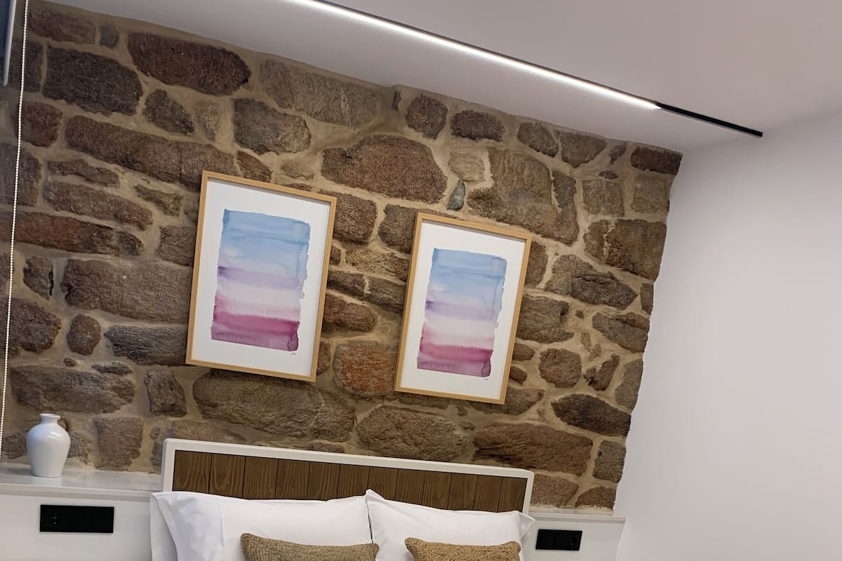 A modern bedroom with a stone wall, a large bed with white bedding, two nightstands, and a pink throw blanket.