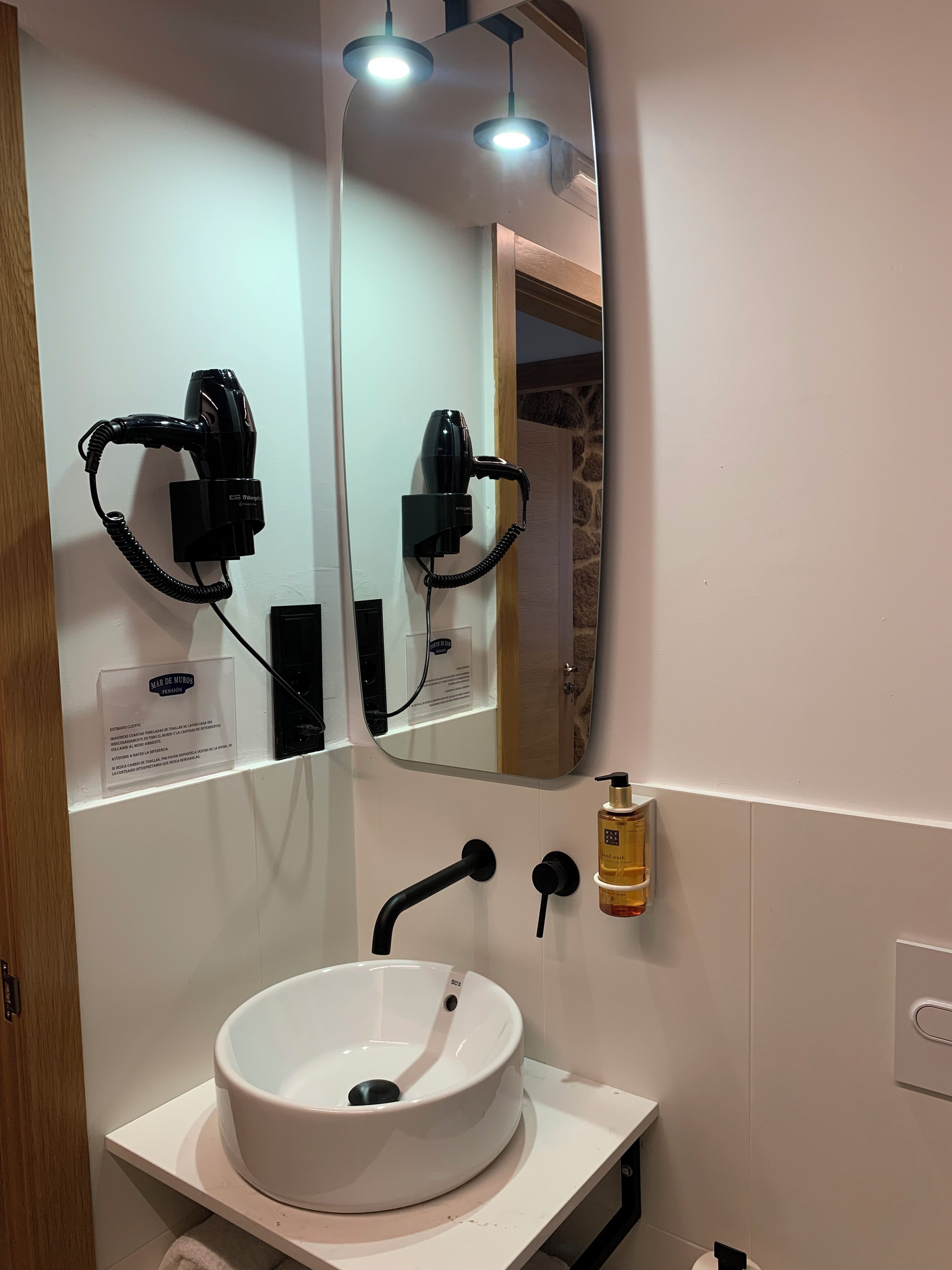 Un baño con un lavamanos blanco, un espejo grande y un secador de pelo montado en la pared.