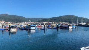 A marina with boats docked, calm water, and a town in the background with hills. - MAR DE MUROS (Muros)