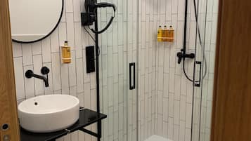A modern bathroom with a glass-enclosed shower, a round mirror, and a sink with a black countertop.
