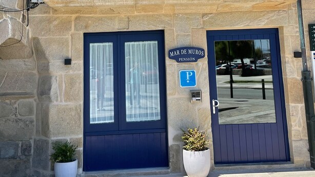 A building with a stone facade, a blue balcony with flower boxes, a blue door, and a parking sign. - MAR DE MUROS (Muros)
