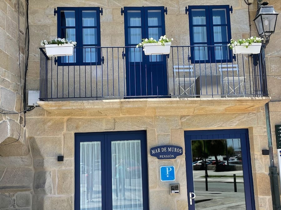 A building with a stone facade, a blue balcony with flower boxes, a blue door, and a parking sign.
