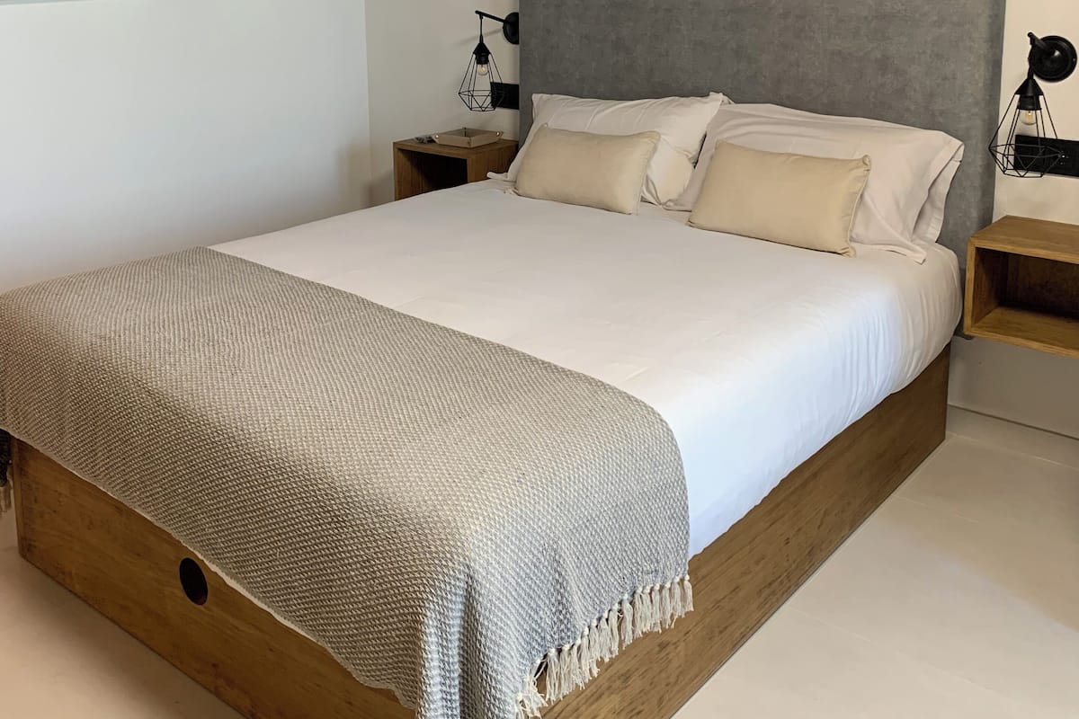 A bedroom with a large bed, wooden headboard, and a nightstand with a lamp.