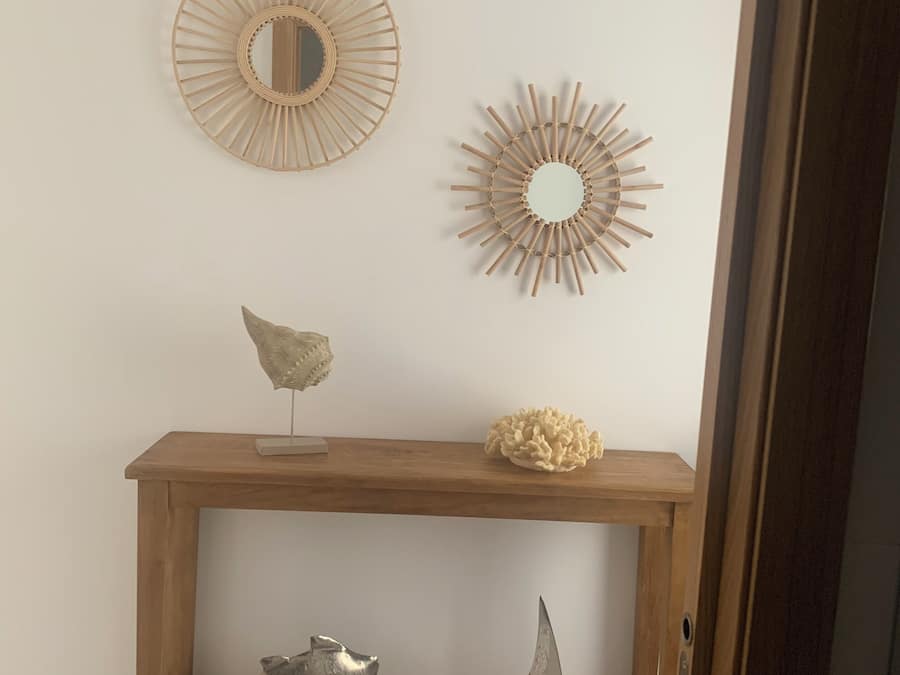 Um console de madeira com objetos decorativos, incluindo um espelho, uma escultura e um modelo de pequeno veleiro.