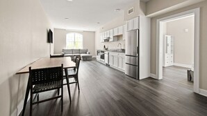 A modern kitchen with white cabinets, a stainless steel refrigerator, and a dining area with a table and chairs. - Charming 1BR Suite in the Heart of New Orleans (New Orleans)