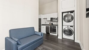 Een ruimtelijke leefruimte met een bank, kitchenette en een voorlader wasmachine.