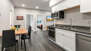 Una cocina moderna con armarios blancos, electrodomésticos de acero inoxidable y un comedor con mesa de madera y sillas negras.