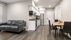 Una cocina moderna con armarios blancos, electrodomésticos de acero inoxidable y un comedor con mesa de madera y sillas negras.