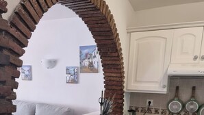 Una cucina compatta con mobili bianchi, un arco in mattoni e un piccolo spazio pranzo con un divano.