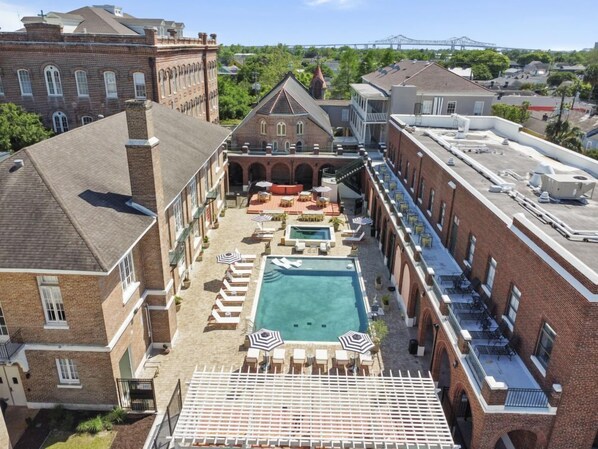 A rooftop pool area with lounge chairs, umbrellas, and a swimming pool surrounded by brick buildings. - Chic 1BR Suite with Local Charm in New Orleans (New Orleans)
