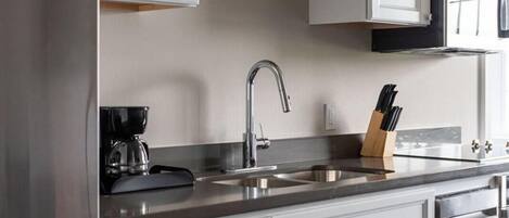 Una cocina moderna con armarios blancos, electrodomésticos de acero inoxidable y una cafetera negra.