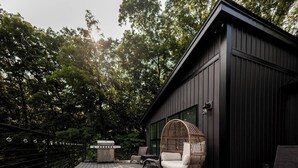 Una terraza de madera con mobiliario exterior, una parrilla y un edificio con revestimiento oscuro.