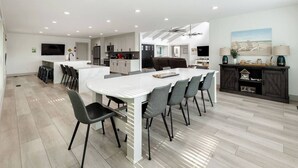 Una cocina moderna con armarios blancos, una isla central y una zona de comedor con sillas grises.