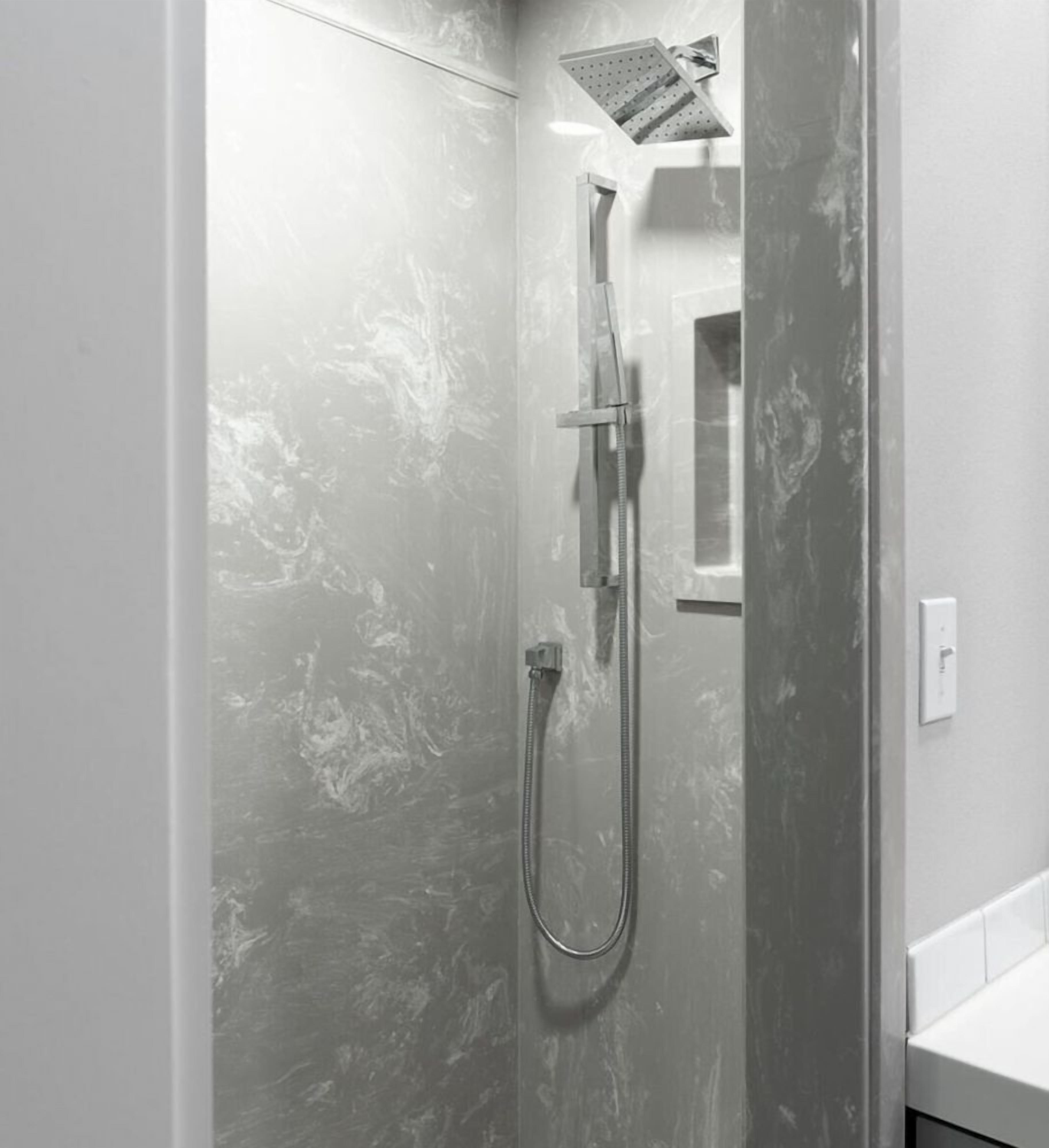 A modern bathroom with a glass-enclosed shower, a handheld showerhead, and a wall-mounted faucet.