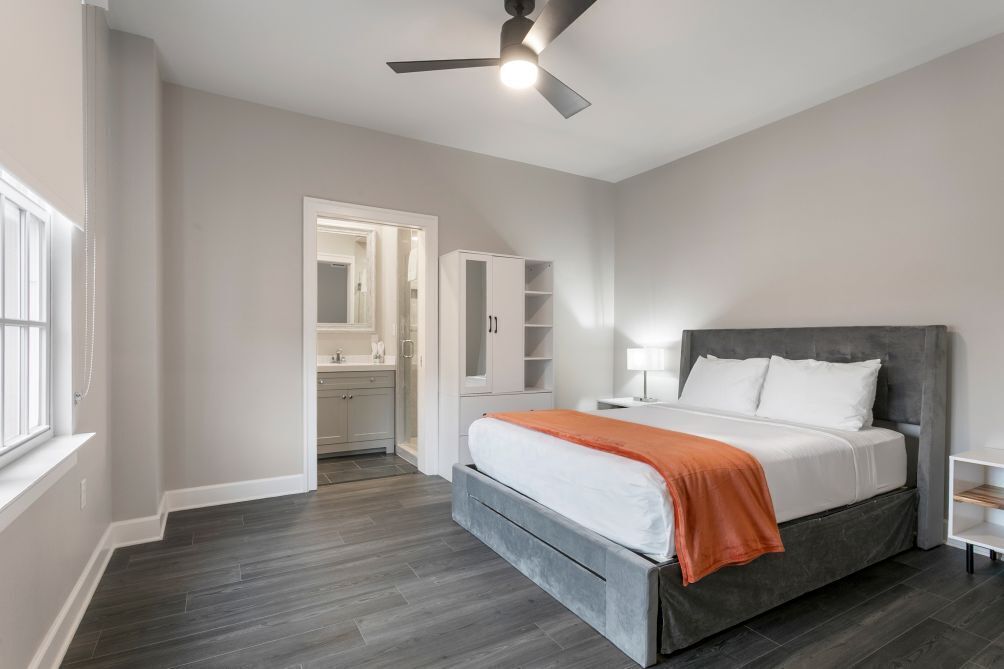 Ein modernes Schlafzimmer mit Bett, Deckenventilator, Nachttisch und begehbarem Kleiderschrank.