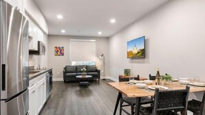 A modern kitchen with white cabinets, a stainless steel refrigerator, and a dining area with a wooden table and black chairs.
