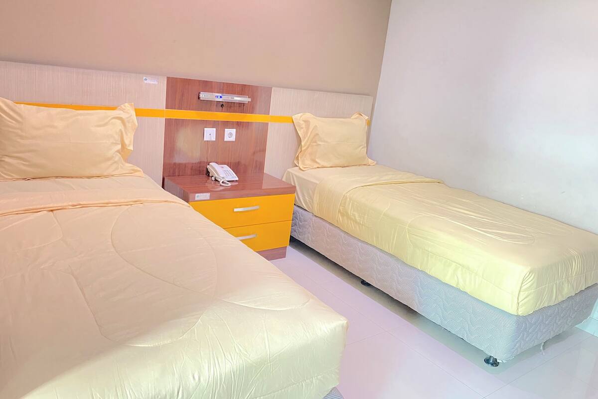 A hotel room with two beds, a wooden headboard, a bedside table with a phone, and a small cabinet.