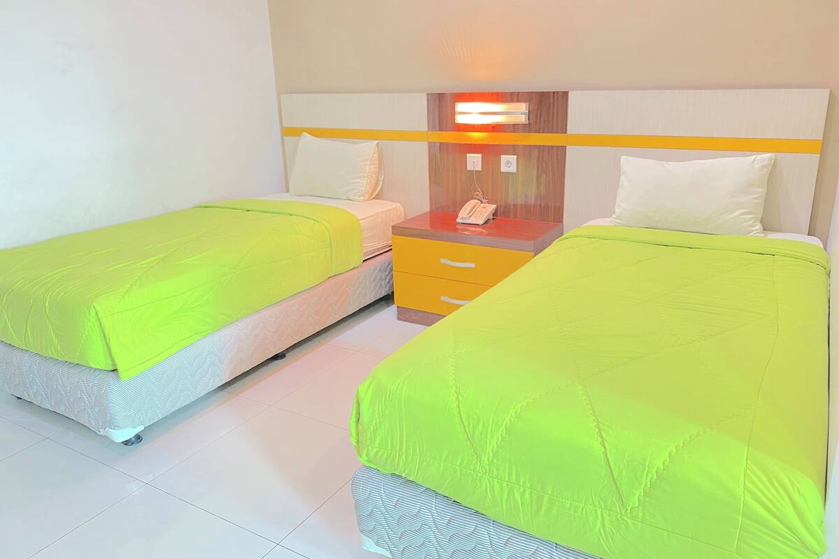 A hotel room with two beds, each with a bright green bedspread, a bedside table with a phone, and a wall-mounted light.