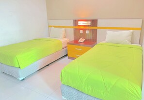 Een hotelkamer met twee bedden, elk voorzien van een felgroene sprei, een nachtkastje met een telefoon, en een wandlamp.