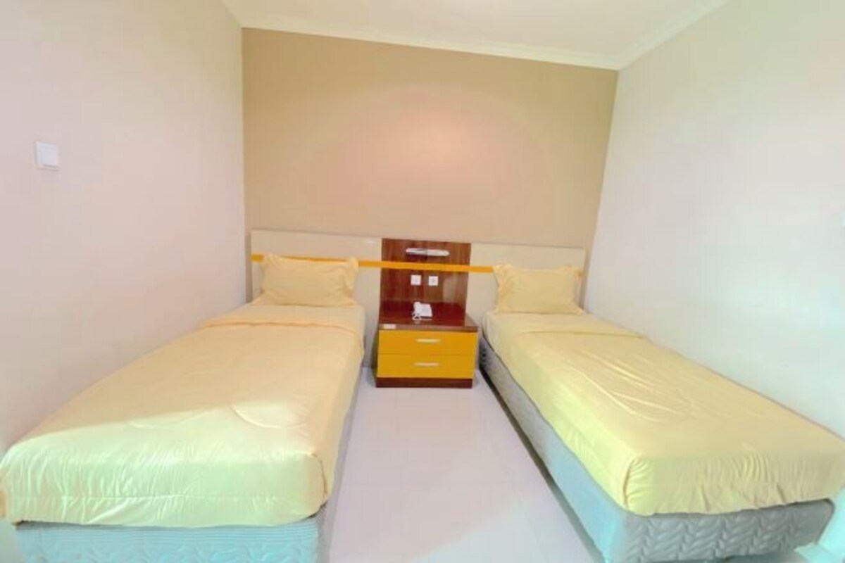 Un dormitorio pequeño de hotel con dos camas individuales, una mesita de noche de madera y una pared sencilla.