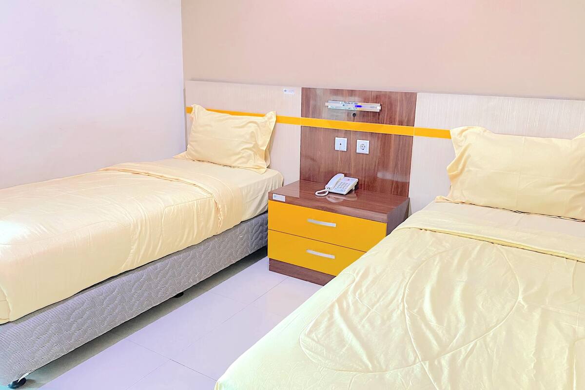 A hotel room with two single beds, each with a yellow bedspread and matching pillows. There is a wooden nightstand with a telephone and a power outlet.