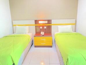 Una habitación de hotel con dos camas individuales, una mesita de noche de madera con un teléfono y una lámpara colgante iluminada.