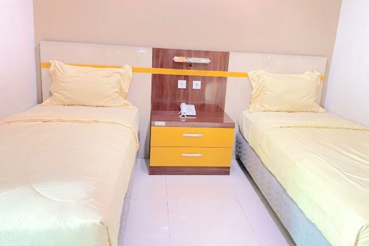 Habitación doble con dos camas, una mesita de noche de madera con teléfono y cabecero amarillo.
