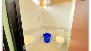 A small bathroom with a bathtub, a toilet, and a shower. There is a blue bucket on the floor.