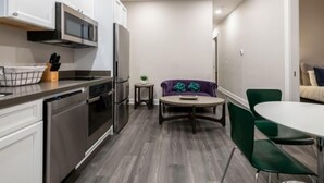 A compact kitchen with modern appliances, a dining area with a round table and chairs, and a small side table with a plant.