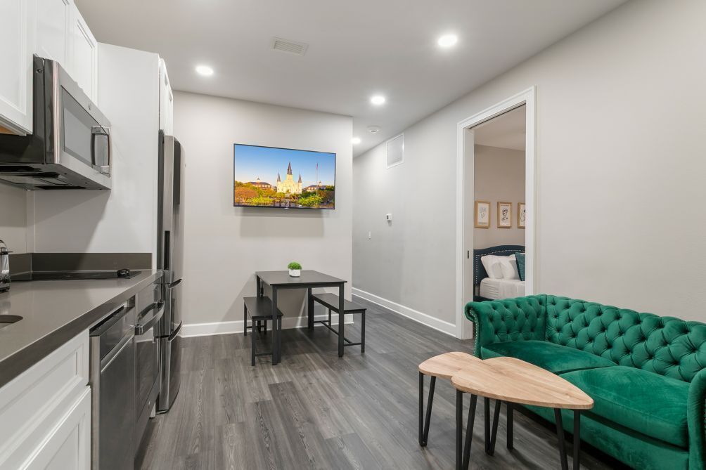 A modern kitchen with stainless steel appliances, a dining area with a table and chairs, and a green sofa.
