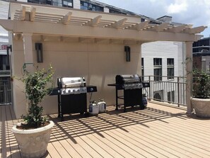 Un patio al aire libre con dos parrillas, plantas en macetas y una estructura de pérgola.