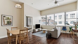 Un salon spacieux comprenant un coin repas, de grandes fenêtres, un ventilateur de plafond et un téléviseur.
