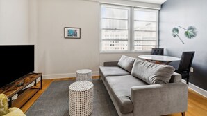 Una sala moderna con un sofá gris, una mesa de centro redonda, dos mesitas auxiliares redondas, un televisor de pantalla plana y un cuadro enmarcado en la pared.