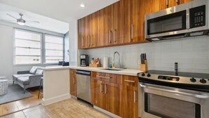 Una cocina moderna con armarios de madera, electrodomésticos de acero inoxidable y un sofá gris en la zona de estar contigua.