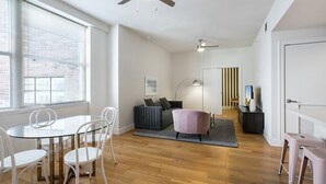 A modern living room with a glass dining table, white chairs, a grey sofa, and a ceiling fan. - Frenchmen Flats Condo: 1BR Peace (New Orleans)