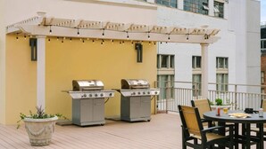 An outdoor patio with two barbecue grills, a round table with chairs, and a pergola with string lights. - Frenchmen Flats Condo: 1BR Peace (New Orleans)