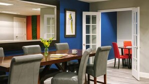 Een vergaderzaal met een houten tafel, grijze stoelen, een bloevas en een lijst met een foto aan de muur.