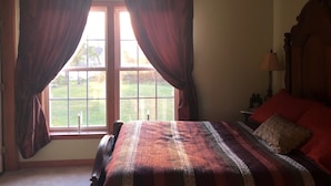 Ein Schlafzimmer mit großem Fenster, einem Bett, einem Nachttisch und einem Deckenventilator.