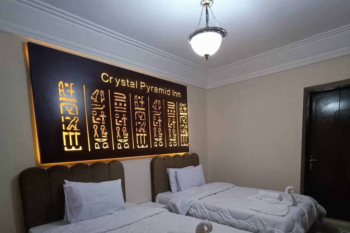 A hotel room with two beds, a wall with hieroglyphics, and a chandelier.