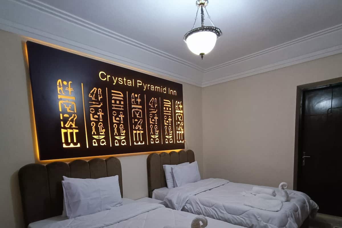 A hotel room with two beds, a wall with hieroglyphics, and a chandelier.