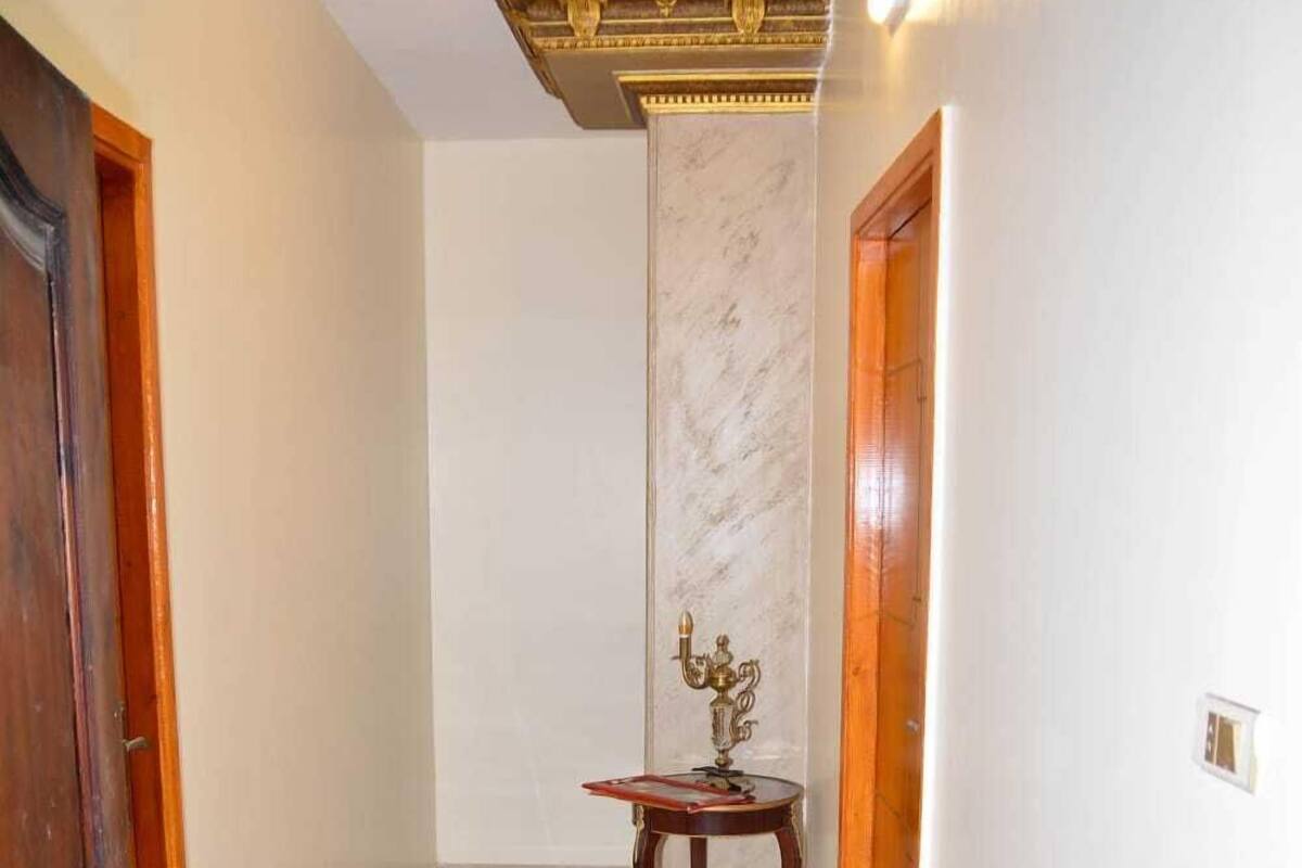 A hallway with marble flooring, a wooden door on the left, and a small table with a decorative item in the center.