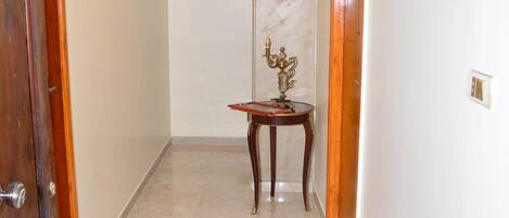A hallway with marble flooring, a wooden door on the left, and a small table with a decorative item in the center.