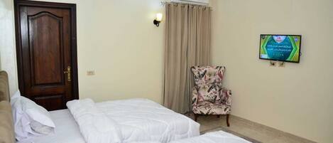A hotel room with two beds, a chair, a TV, and a door.