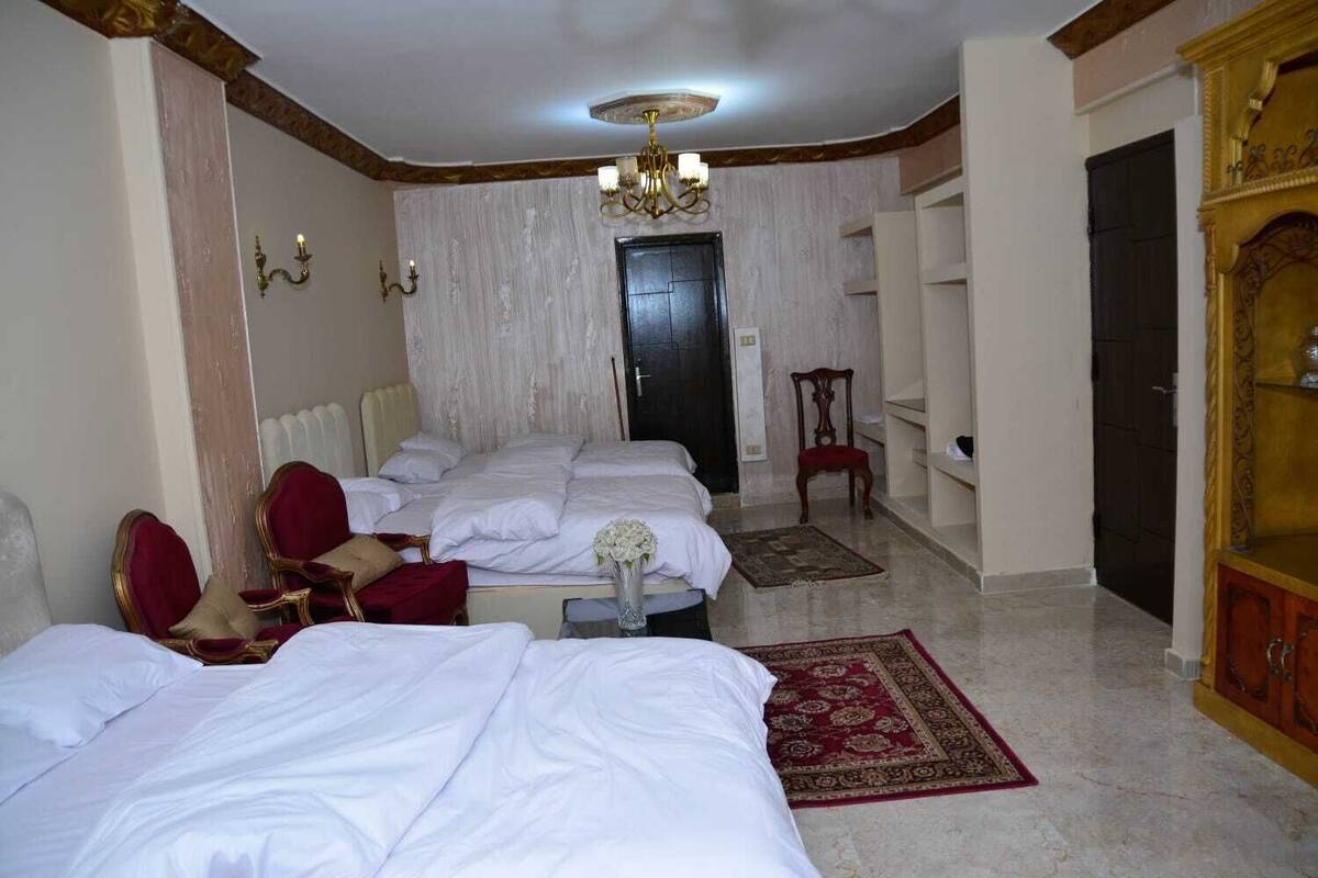 A hotel room with three beds, a chandelier, a red chair, and a wooden cabinet.