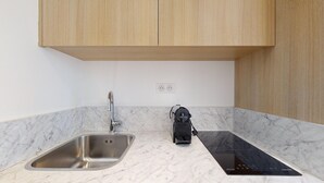 A kitchen with a stainless steel sink, a black induction cooktop, and wooden cabinets. - TBS 167 - Refined and bright studio (Paris)