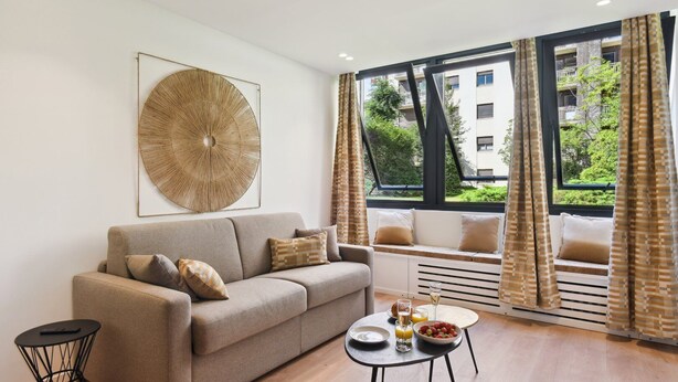 A modern living room with a sofa, a coffee table, and a large window with curtains.