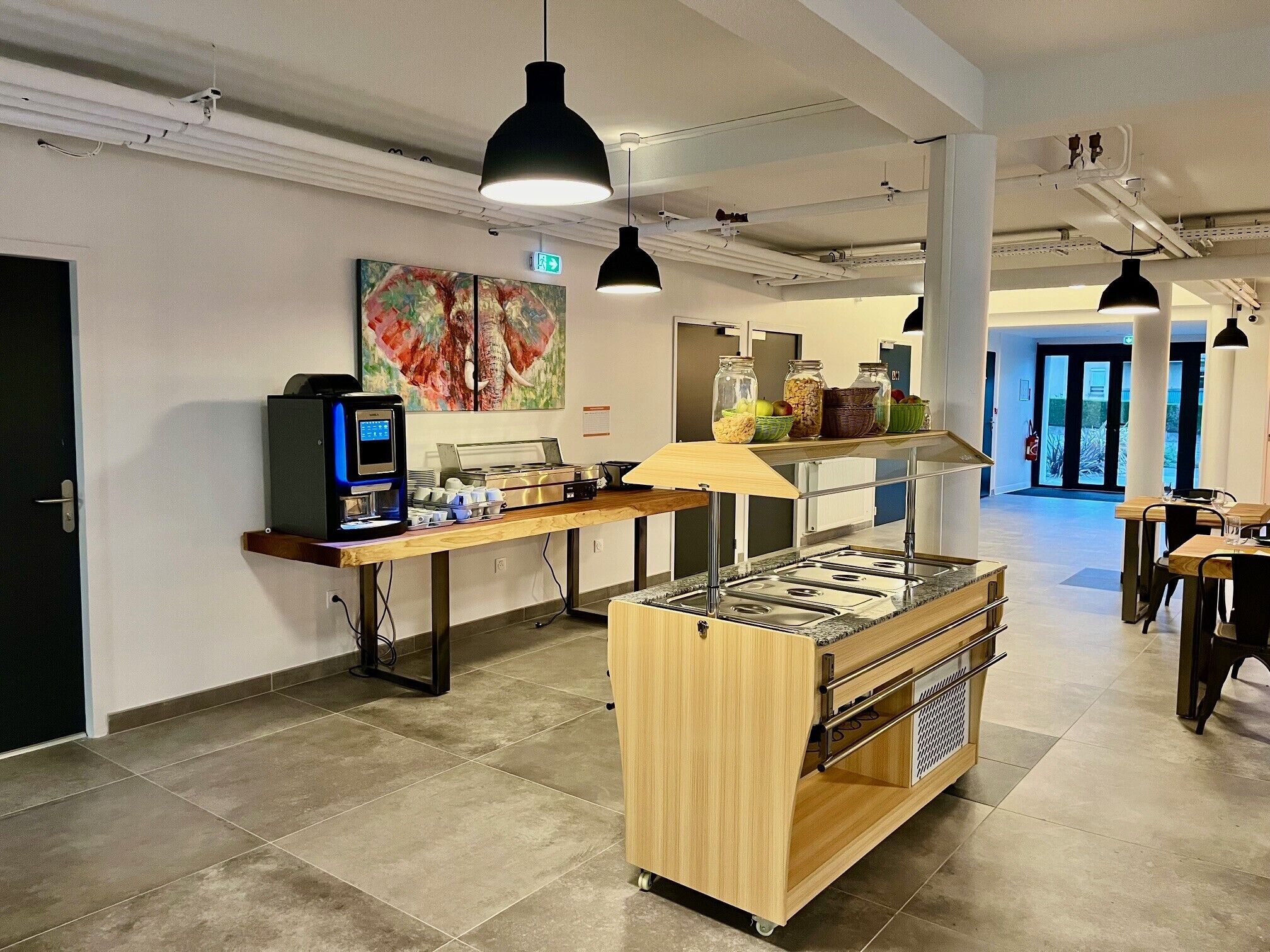 A modern cafe with a coffee machine, a buffet counter, and a painting on the wall.